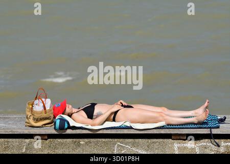 France, Seine Maritime, Veules les Roses, Young woman lying on a bench along the pebble beach promenad Stock Photo