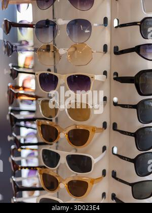 A selection of fashionable sunglasses is arranged on a display rack. The diverse styles include different shapes and shades, appealing to various tast Stock Photo