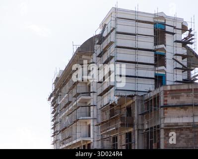 Workers are busy on a multi-story building construction site surrounded by scaffolding. The structure shows progress with newly installed windows and Stock Photo