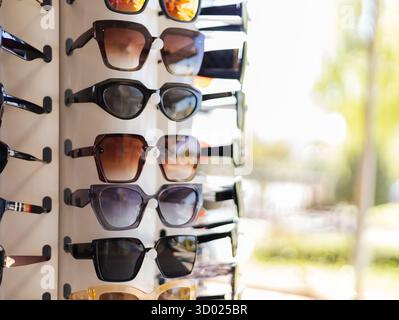 A selection of stylish sunglasses hangs on a display rack. The sun shines brightly, highlighting the different shapes and colors. The setting suggests Stock Photo