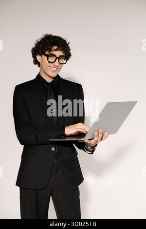 Stylish man in a black suit interacts with a laptop, blending fashion and technology. Stock Photo