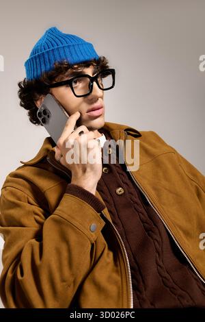 Young handsome man wearing a blue hat and stylish jacket engages in conversation while pondering. Stock Photo