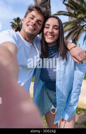 Happy couple taking selfie together at the beach with palm trees in background Stock Photo