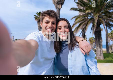 Happy couple taking selfie together at the beach with palm trees in background Stock Photo