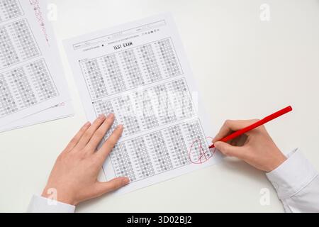 Female teacher writing results in answer sheets form of school test on white background Stock Photo