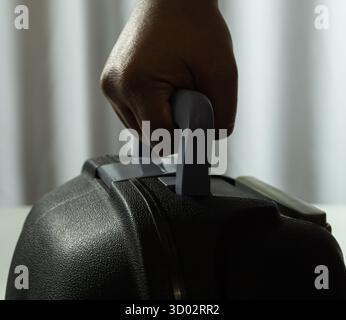 Close-up of suitcase being lifted by hand, set against white fabric background, travel concept with modern luggage design and clean minimalist present Stock Photo
