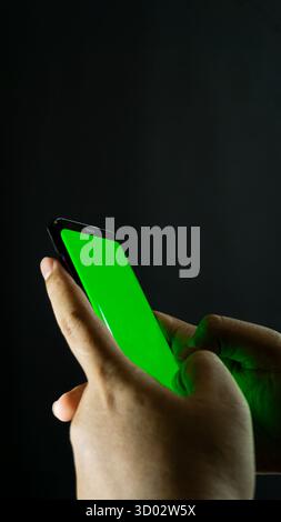 Two hands typing on smartphone with green screen, angled side view on black background, perfect for UI mockup or touchscreen interaction concept Stock Photo
