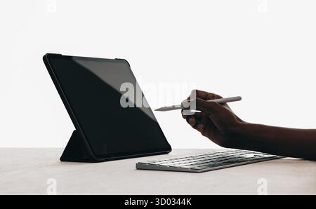 Modern workspace setup featuring a tablet on a stand, keyboard, and a hand using a stylus in a minimal setting, emphasizing technology, creativity, an Stock Photo