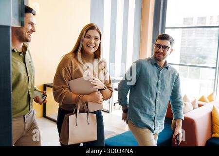 Three colleagues walking together in a modern office, depicting teamwork and positivity. Joyful expressions highlight their professional connection in Stock Photo