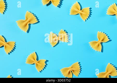 Uncooked bow tie pasta, farfalle scattered on a blue background in a decorative pattern, emphasizing texture and shape Stock Photo