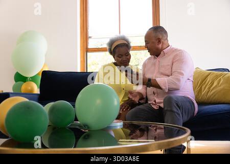 Sharing joyful moment, African American senior couple using smartphone on sofa. Technology, connection, happiness, elderly, lifestyle, retirement || Model released Stock Photo