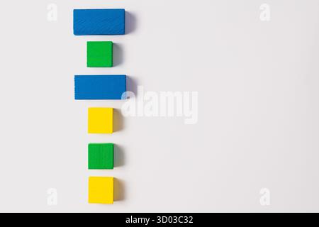 Blue, green, and yellow rectangular and square wooden blocks arranged in a vertical pattern on a plain white surface. Stock Photo