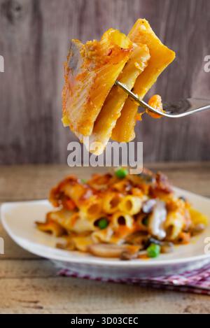 Rigatoni pasta baked with pumpkin, mushrooms, peas, and melted cheese on a white plate Stock Photo