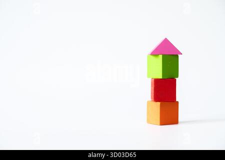 Three colorful wooden cubes in orange, red, and green stacked vertically, topped with a pink triangle block to resemble a house, isolated on white bac Stock Photo