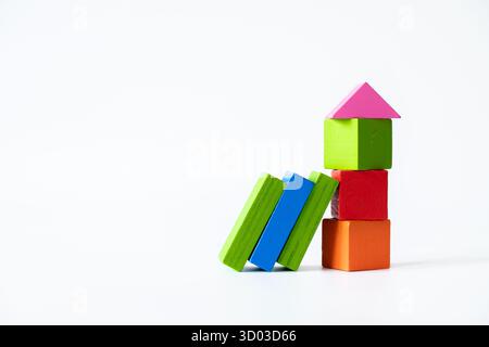 Colorful wooden toy blocks stacked vertically to resemble a house, with additional green and blue blocks leaning sideways, all isolated on a white bac Stock Photo