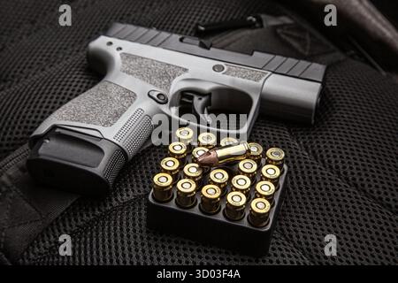 A compact two-tone pistol and ammunition on a dark tactical gear background. Stock Photo