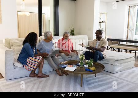 Family in living room using digital devices and having conversation together. lifestyle, technology, bonding, leisure, connection, communication || Model released Stock Photo