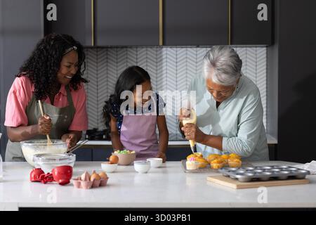 Three generations baking cupcakes together in modern kitchen, sharing joyful moments. Family, togetherness, bonding, cooking, happiness, celebration || Model released Stock Photo
