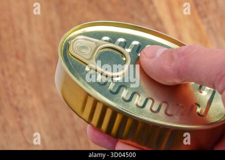 Metal can of preserved tuna fish in man hand over wooden table close up Stock Photo