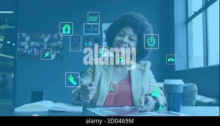 Reviewing woman wearing blazer pointing pen at charts in modern office, with sustainability icons Stock Photo