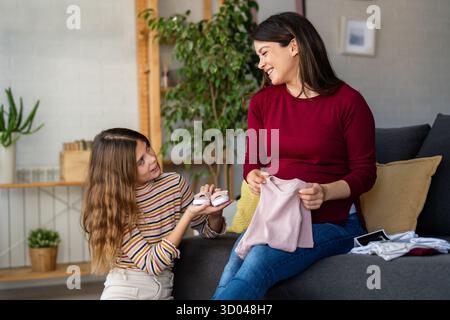 Heartwarming family moment as expectant mom and son joyfully browse through newborn baby's clothes Stock Photo