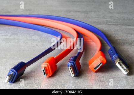 Close-up of red and blue USB, Micro USB, and USB-C charging cables on a gray surface, symbolizing tech, data transfer, and connectivity Stock Photo