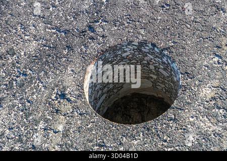 A close-up view of a core-drilled hole in asphalt pavement used for testing thickness, density, and quality of road construction material Stock Photo