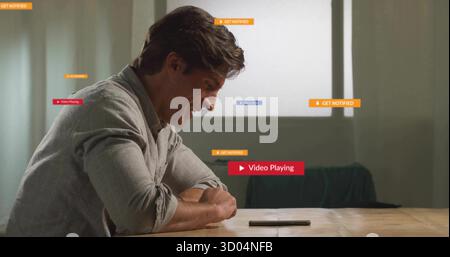 Leaning man wearing shirt smiling at smartphone on wooden table in living area with notifications Stock Photo