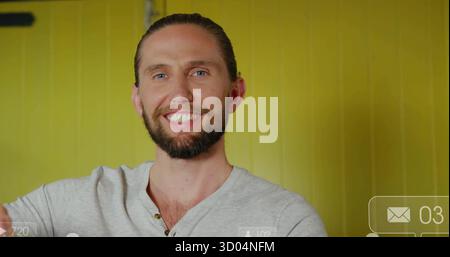 Smiling bearded man looking at camera in studio on yellow wall, showing digital overlay elements Stock Photo