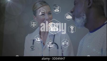 Consulting female doctor using stethoscope with patient in gown in clinic, with floating icons Stock Photo
