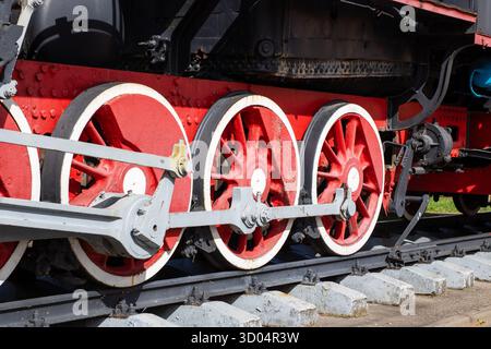 Detailed view of old steam locomotive wheels painted red, showcasing the historical engineering of trains on railway tracks. Stock Photo