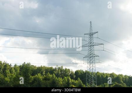 Russia, Saint Petersburg, 23.08.2025 Electricity pylon with high voltage lines extending across a cloudy sky, standing tall above a lush green forest, Stock Photo