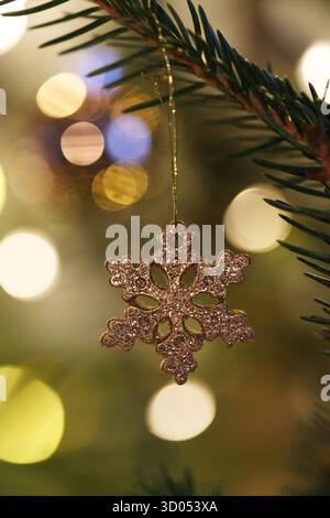 Sparkling, glittery snowflake ornament hanging on a Christmas tree with bright, warm bokeh lights in the background Stock Photo
