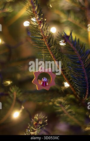 Small, wooden ornament with a tiny angel figure inside hanging on Christmas tree with warm, bokeh lights in the background Stock Photo