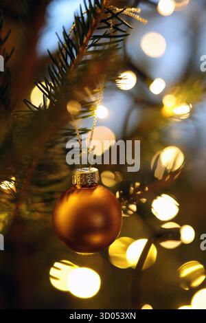 Matte golden bauble hanging from a Christmas tree branch by warm bokeh lights in the background Stock Photo
