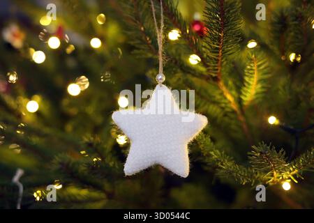 White, soft, star-shaped ornament hanging from a Christmas tree with warm blurred bokeh lights in the background Stock Photo