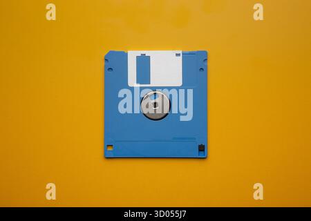Blue 3.5-inch floppy disk centered on a vibrant yellow background Stock Photo