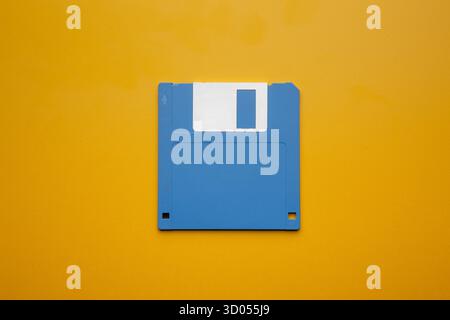 Blue 3.5-inch floppy disk centered on a vibrant yellow background Stock Photo