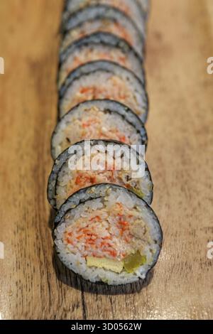 Neatly sliced Korean Kimbap (seaweed rice rolls) featuring rice, tuna, and crab stick filling, served on a wood board. A popular, healthy Asian lunch. Stock Photo