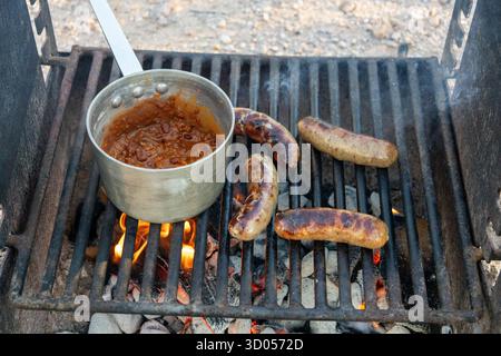 Bratwurst Sausages and Chili Cooking on Campfire Grill with Flames and Coals Outdoors Stock Photo