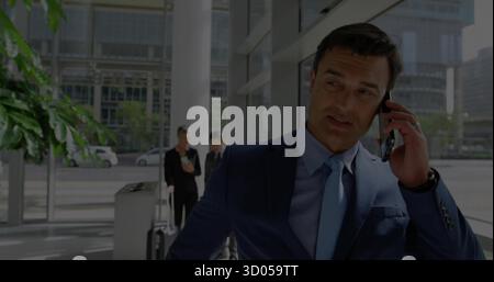 Talking Asian businessman wearing navy suit using smartphone in lobby with glass wall, copy space Stock Photo