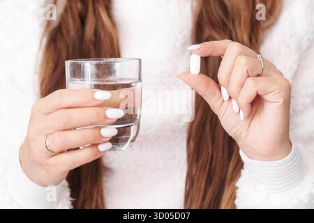 Woman holding glass of water and pill. Concept of taking medicine, supplements or vitamins for health care and wellness routine. Stock Photo