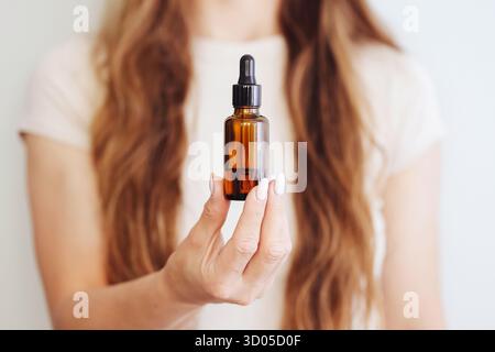 Woman holding amber dropper bottle. Skincare serum product display. Natural cosmetics in hand. Beauty routine concept. Minimal studio background. Stock Photo