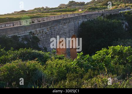 Historic stone bridge along Victoria Lines in Malta, glowing arches at sunset, green valley and shrubs in foreground Stock Photo