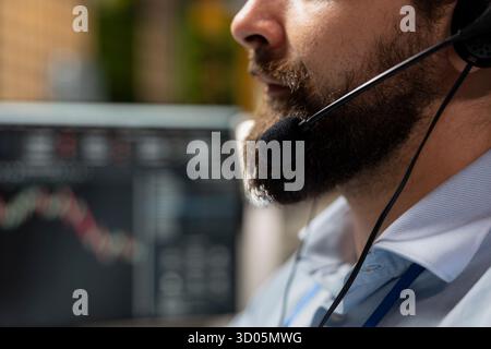 Close up of stockbroker in office speaking in audio headset mic, working with clients to develop investing strategies. Consultant chatting with customers, recommending stock exchange recommendations Stock Photo