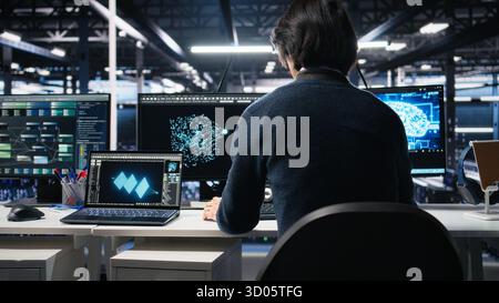 Admin entering data center office, reviews AI diagnostics on computer. IT expert starting work at server farm desk, optimizing artificial intelligence systems configuration, camera A Stock Photo