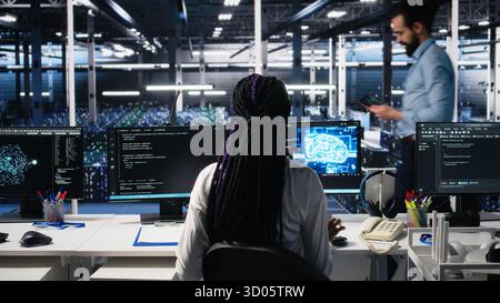 Female programmer in data center reviews AI diagnostics, analyzing neural network performance. Server hub IT expert optimizes artificial intelligence systems configuration, camera A Stock Photo