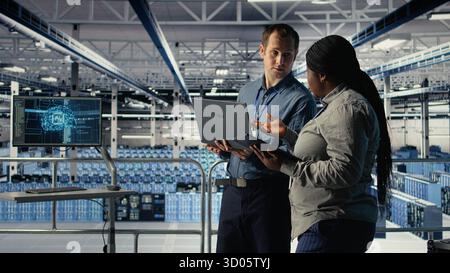 Technicians working together in server room, optimizing deep learning AI systems handling tasks. Data center coworkers doing brainstorming to adjust artificial intelligence model parameters, camera A Stock Photo