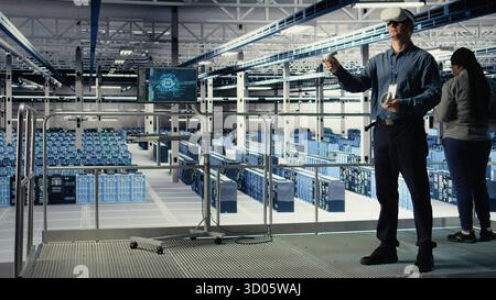 Programmer in server room wearing VR headset optimizing deep learning systems handling tasks. Data center IT specialist adjusting AI model parameters using virtual reality, camera A Stock Photo