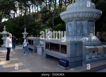 BUSAN, SOUTH KOREA - OCTOBER 9, 2025 - Worshippers praying and walking around the Buddhist stone statues at Haedong Yonggungsa Temple Stock Photo